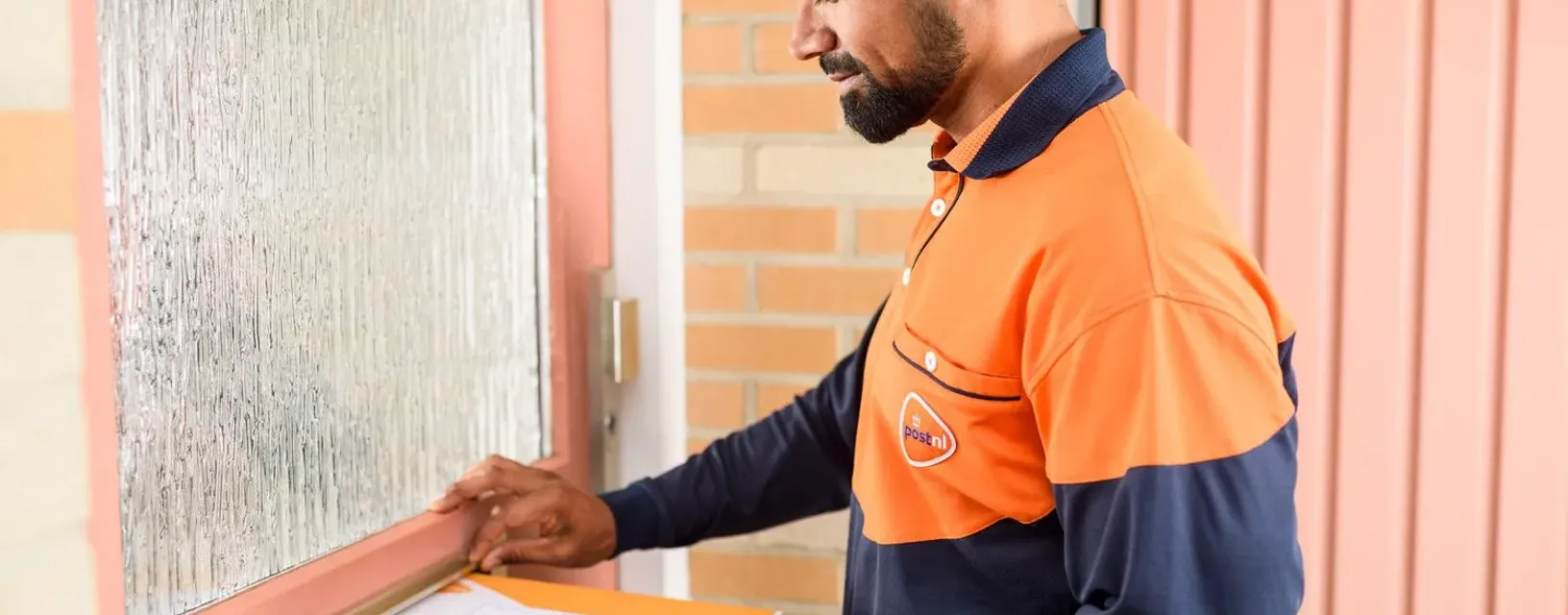 Brievenbuspakketje wordt door de brievenbus gedaan door bezorger PostNL