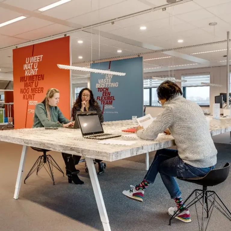 3 collega's werken aan lang bureau