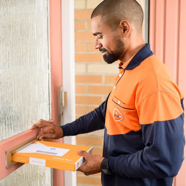 Brievenbuspakketje wordt door de brievenbus gedaan door bezorger PostNL